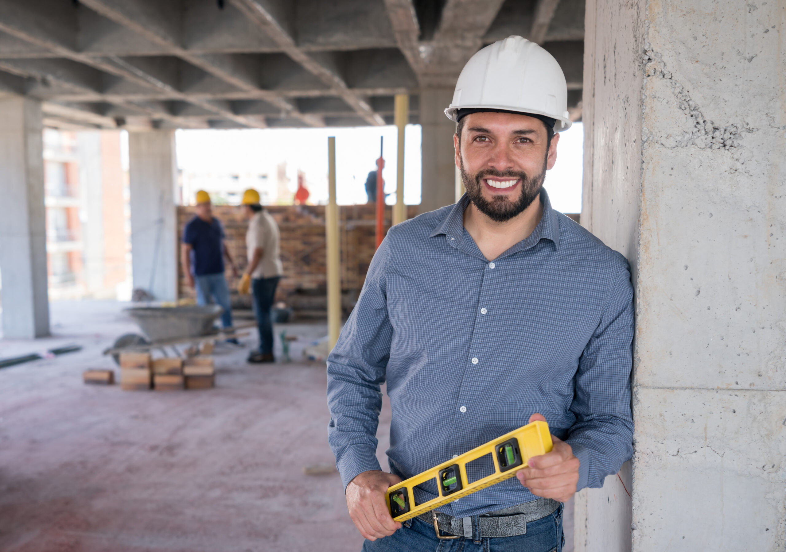 Portrait of a happy engineer at a construction site holding a level tool and looking at the camera smiling