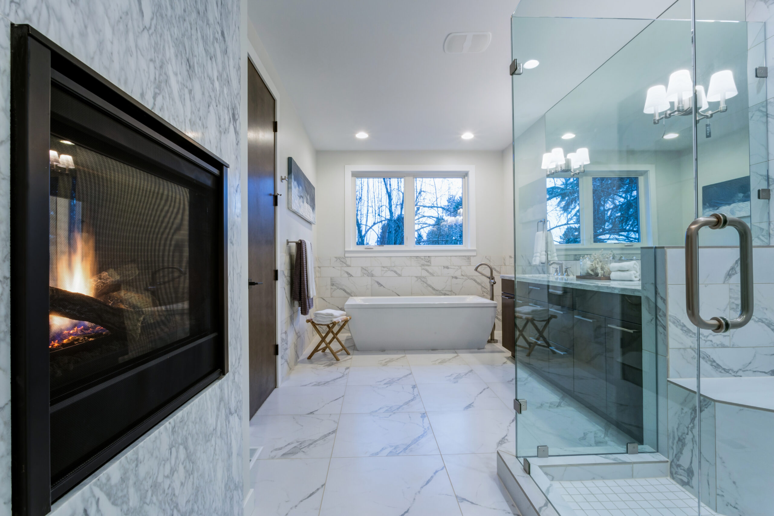 Incredible master bathroom with fireplace, Carrara marble tile surround, modern glass walk in shower, espresso dual vanity cabinet and a freestanding bathtub.